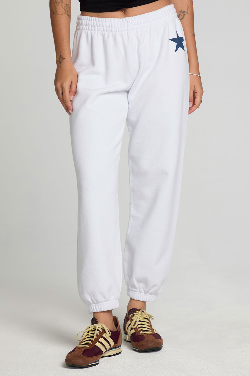 Front view of a woman wearing the Chaser  High Spirits Pants on a neutral background and arms at sides with sneakers