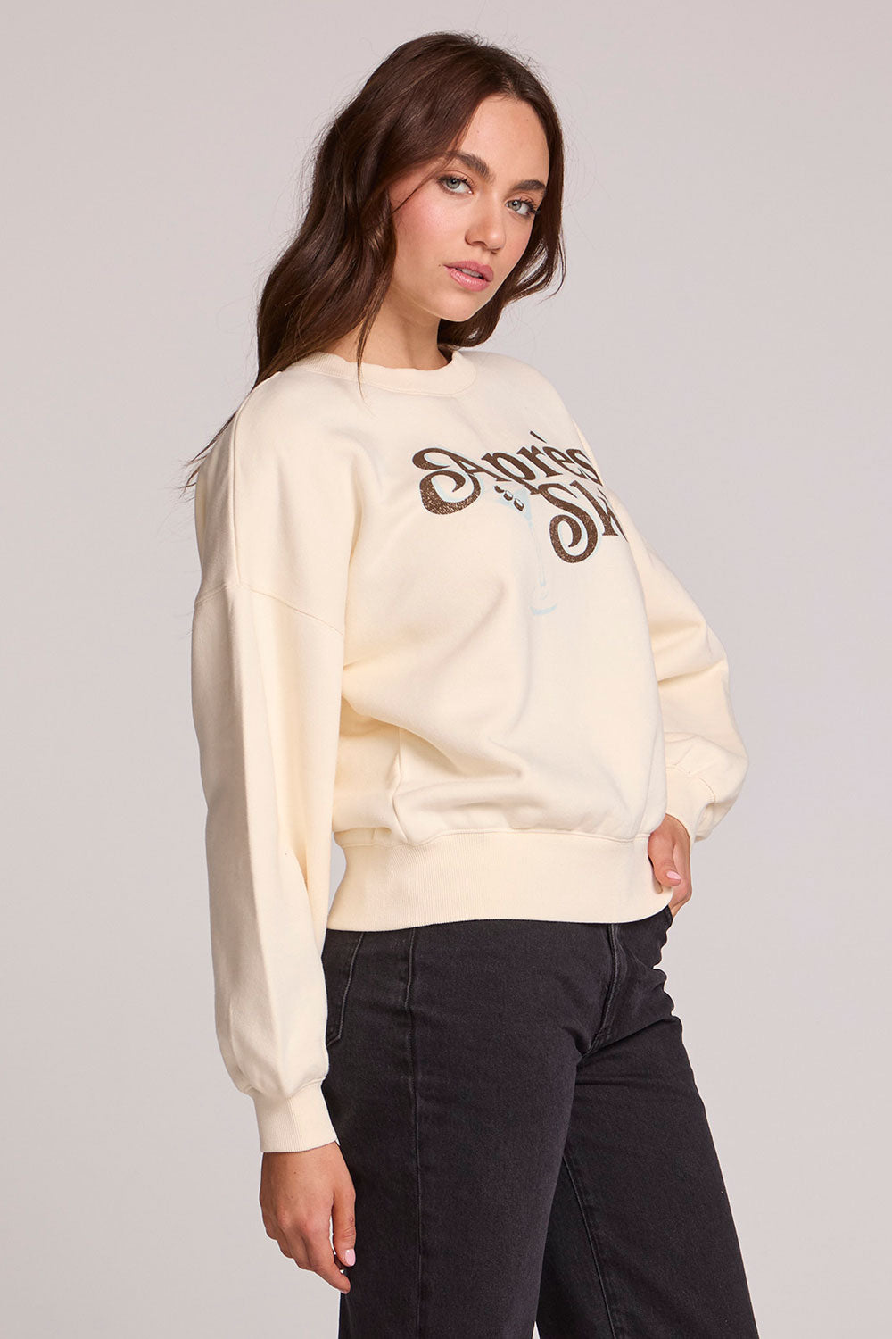 Side angle view of a woman wearing the Chaser How's Your Ap Res Sweatshirt on a neutral background with black pants