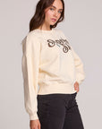Side angle view of a woman wearing the Chaser How's Your Ap Res Sweatshirt on a neutral background with black pants
