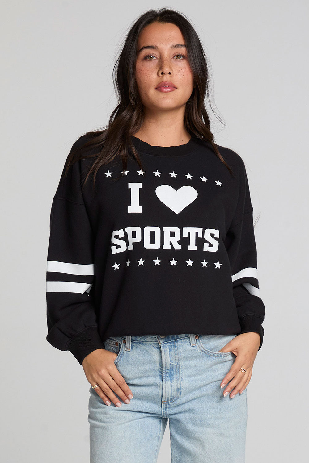 Front view of a woman wearing the Chaser I Love Sports Sweatshirt on a neutral background with hands on pockets