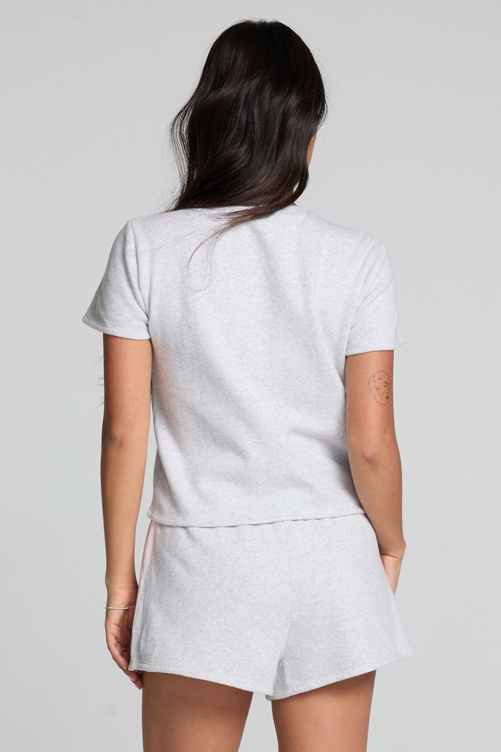 Back view of a woman wearing the Chaser  Isla Light Heather Grey Tee and matching shorts on a neutral background
