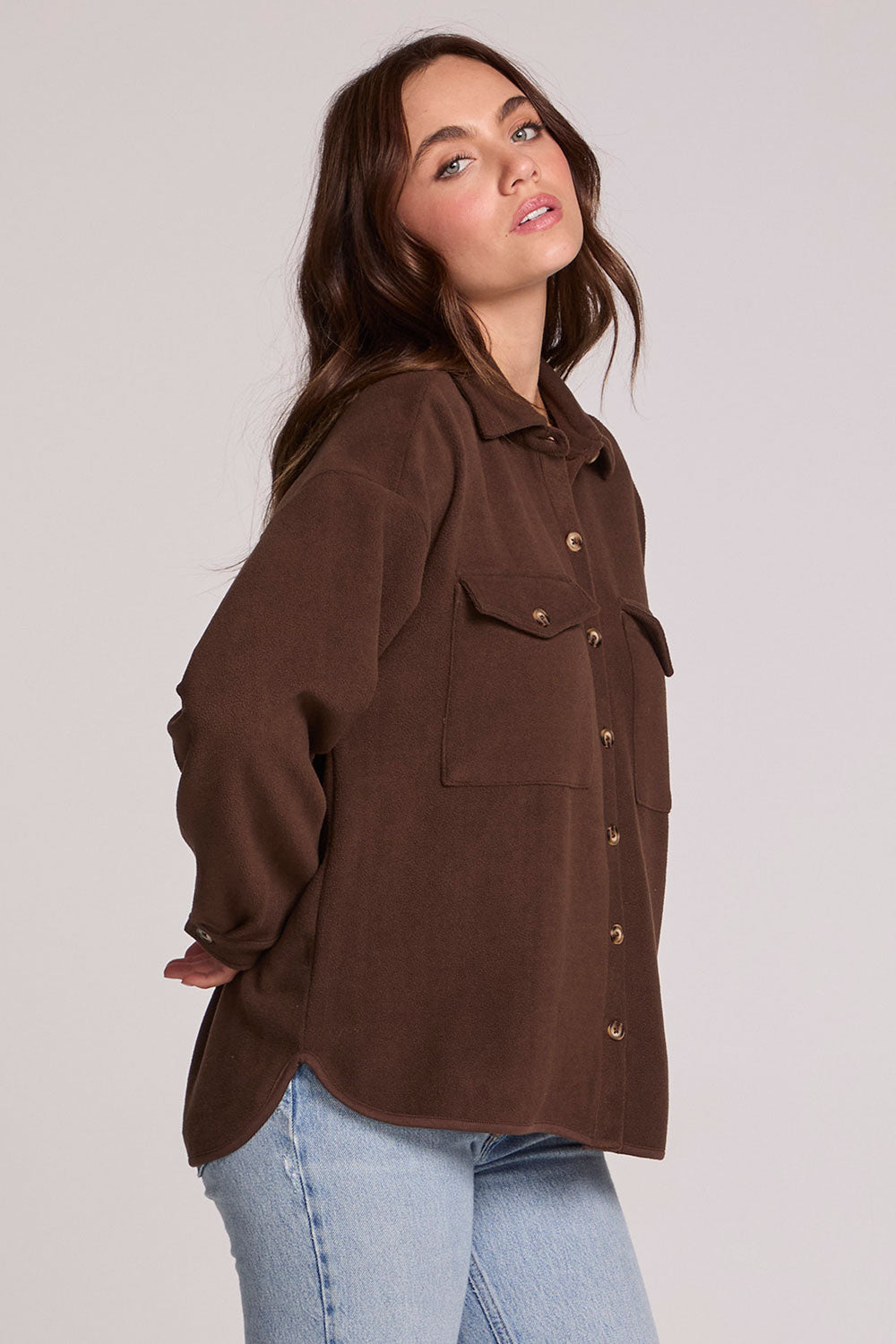 Side angle view of a woman wearing the Chaser Jaxxon Wood Brown Shacket on a neutral background with arms at back