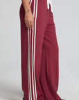 Side angle view of a woman wearing the Chaser Jessee Brick Red Trackpants on a neutral background with arms lowered at sides