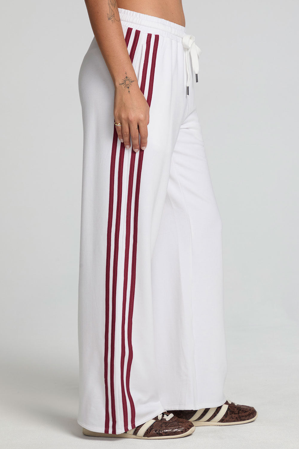 Side view of a woman wearing the Chaser Jessee Cloud White Trackpants on a neutral background with arms down