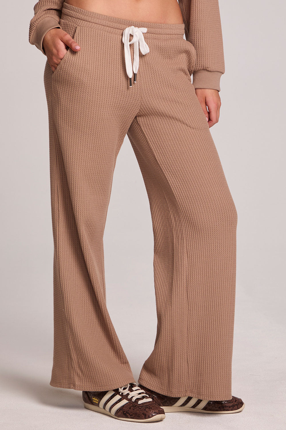 Front view of a woman wearing the Chaser Jorgia Camel Pants on a neutral background with shoes and hands in pocket