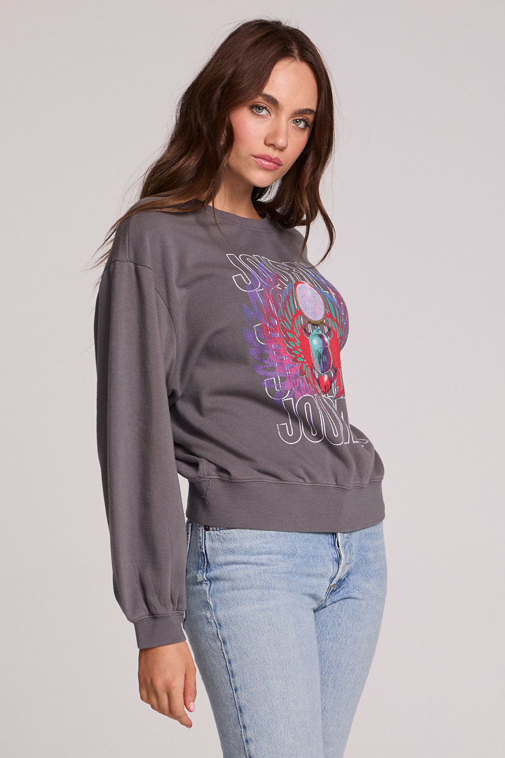 Side view of a woman wearing the Chaser Journey 1983 Tour Sweatshirt on a neutral background with bluejeans
