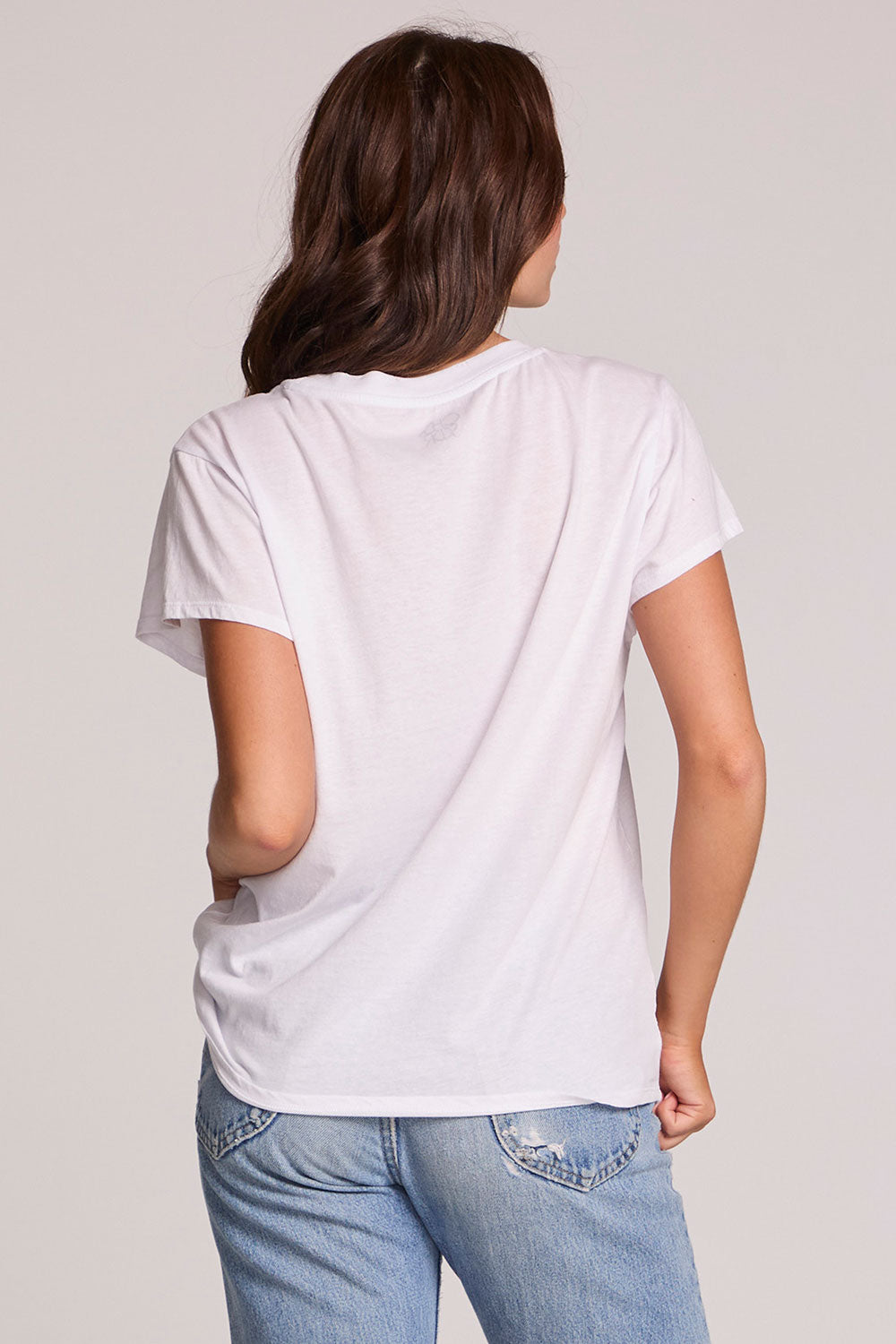 Back view of a woman wearing the Chaser Journey 79 Tour Tee on a neutral background with one handson her hips