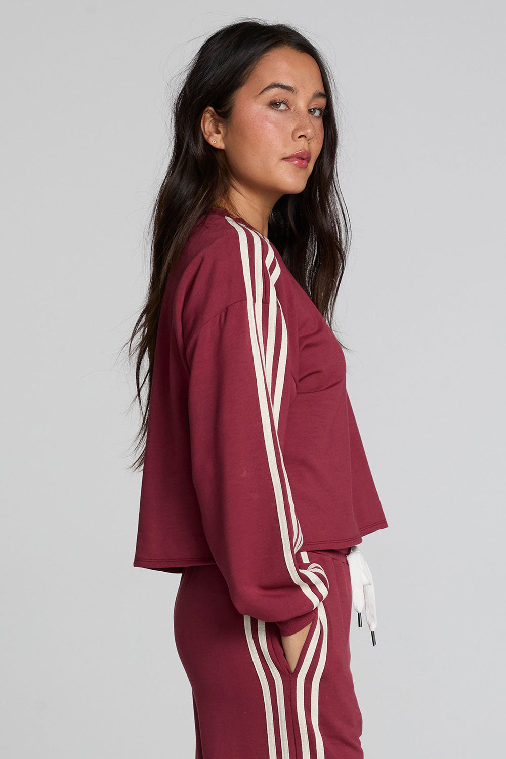 Side view of a woman wearing the Chaser Kloud Burnt Red Sweatshirt on a neutral background with matching pants