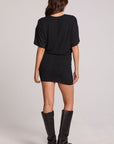 A full body back view of a woman wearing the Chaser Lenora Black Dress on a neutral background with black boots