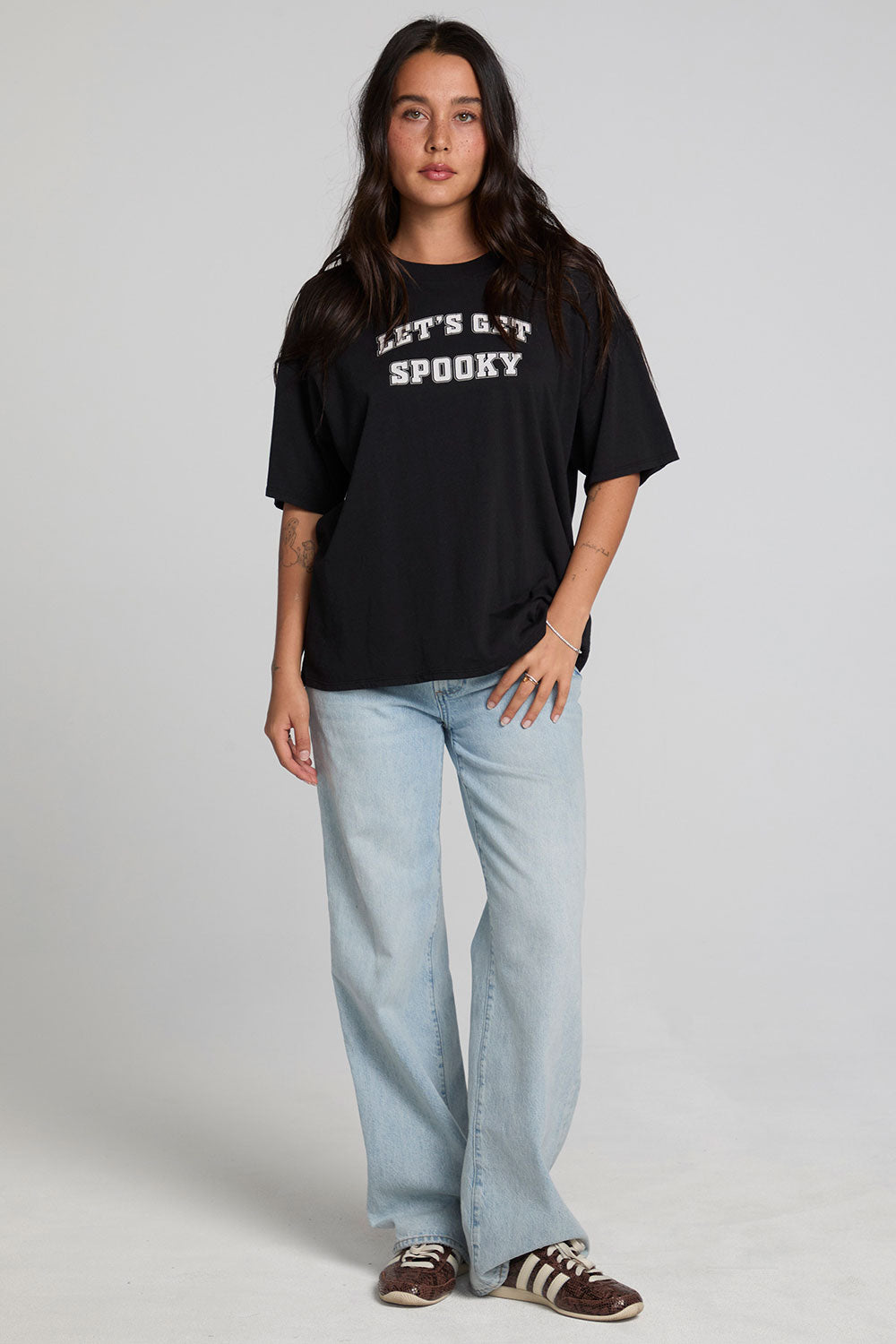 A full body front view of a woman wearing the Chaser Let's Get Spooky Tee on a neutral background