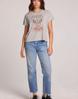 Full body front view of a woman wearing the Chaser  Live Music Graphic Tee and blue jeans on a neutral background with hands lowered