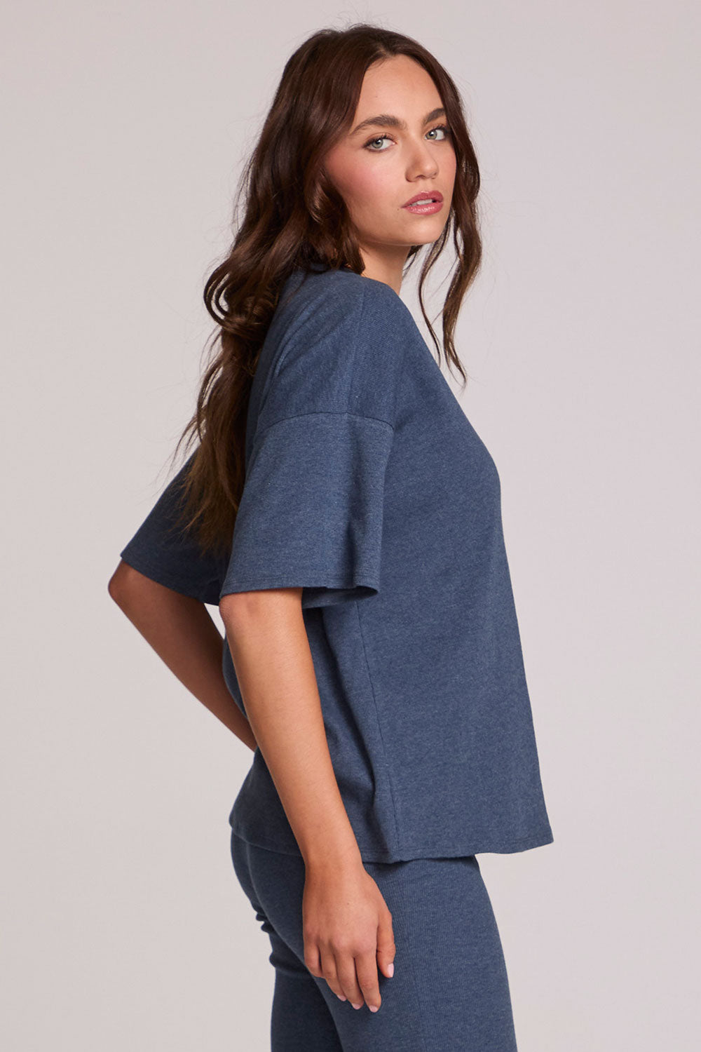 Side angle view of a woman wearing the Chaser Lunnah Dark Denim Top and blue pants on a neutral background 