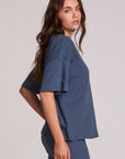 Side angle view of a woman wearing the Chaser Lunnah Dark Denim Top and blue pants on a neutral background 