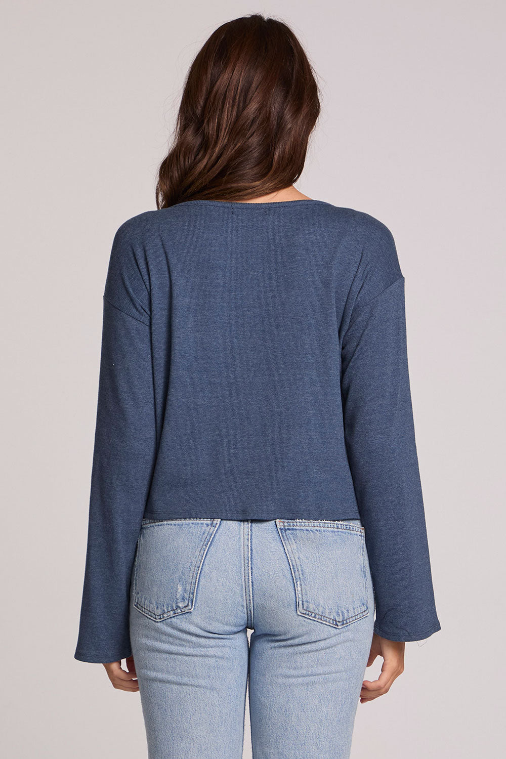 Back view of a woman wearing the Chaser Lunnah Dark Denim Top and blue jeans on a neutral background 