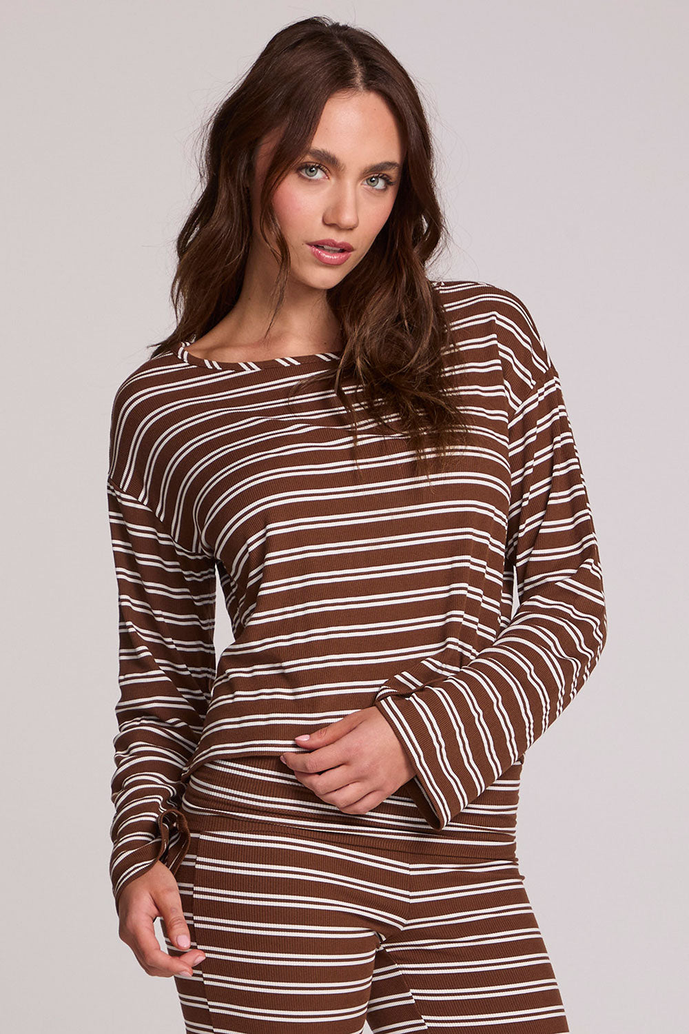 Front view of a woman wearing the Chaser Lunnah Nutty Brown Top and matching striped pants on a neutral background with arm on torso