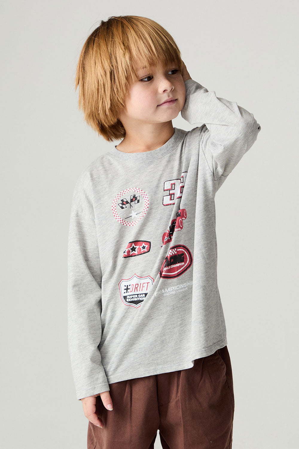 Front view of a boy wearing the Chaser Moto Patches Boys Tee on a neutral background with one hand on face