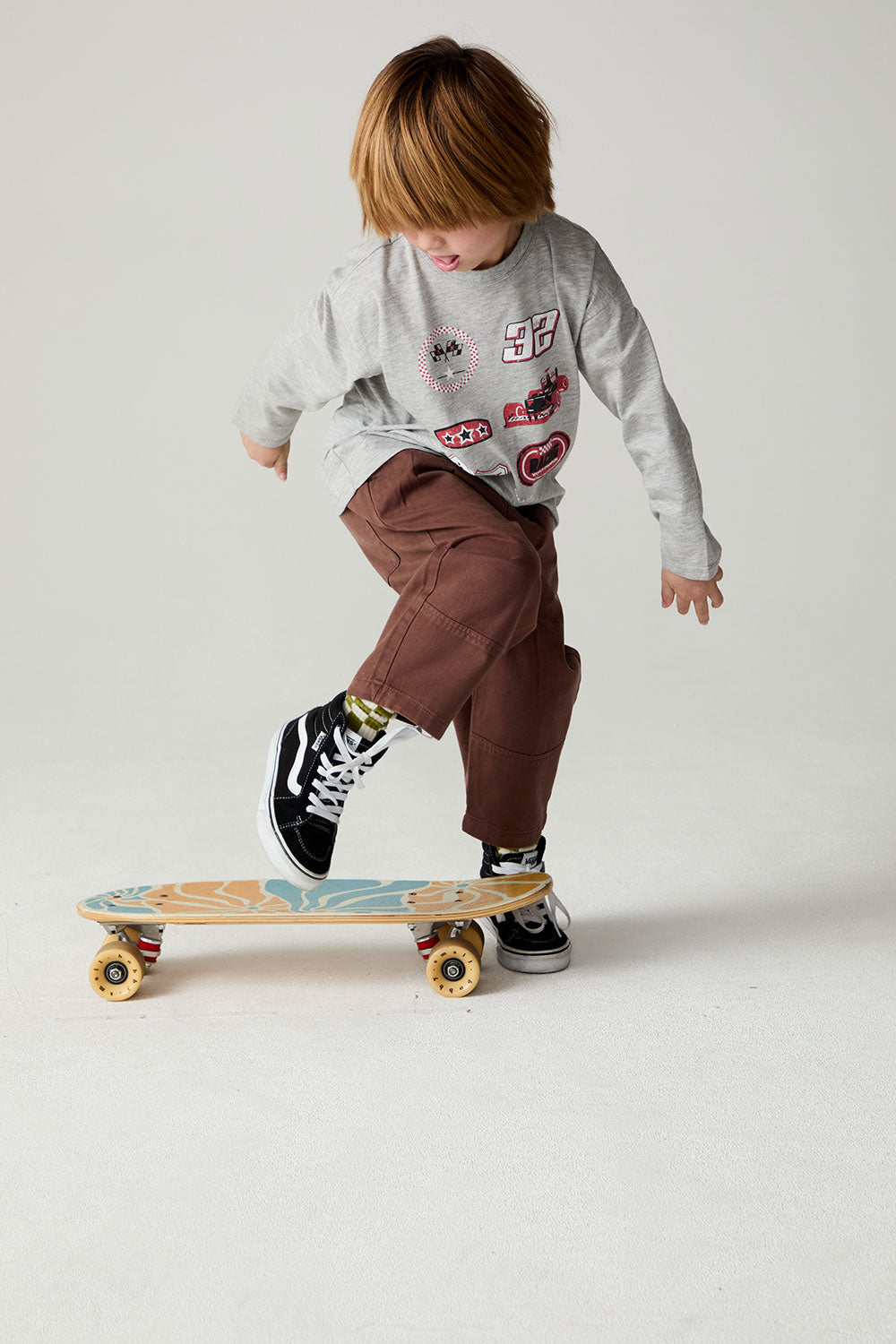 Boy riding a skateboard while wearing the Chaser Moto Patches Boys Tee on a neutral background 