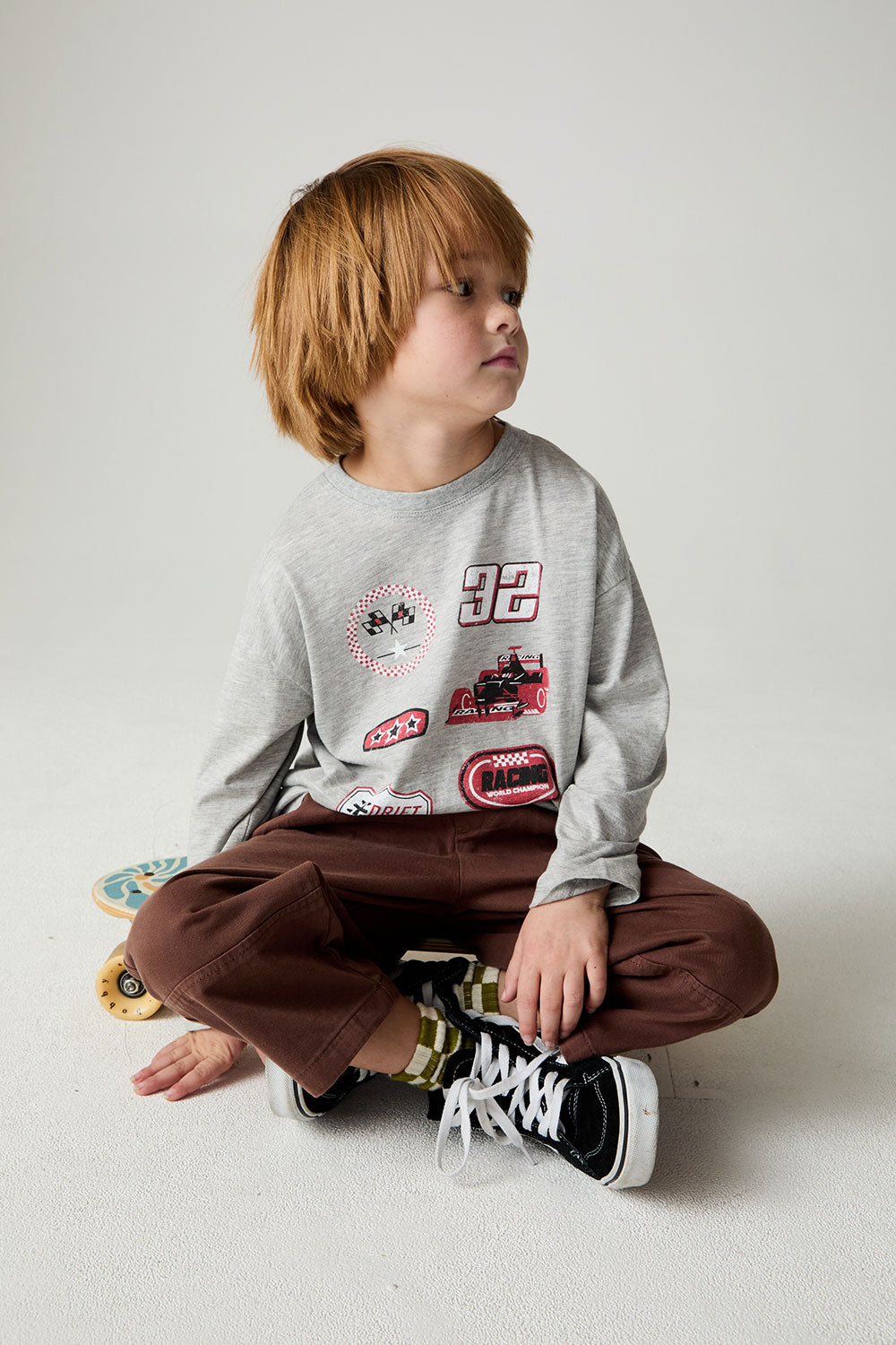 Seated boy wearing the Chaser Moto Patches Boys Tee on a neutral background 