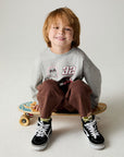 Seated boy on skateboard wearing the Chaser Moto Patches Boys Tee on a neutral background 