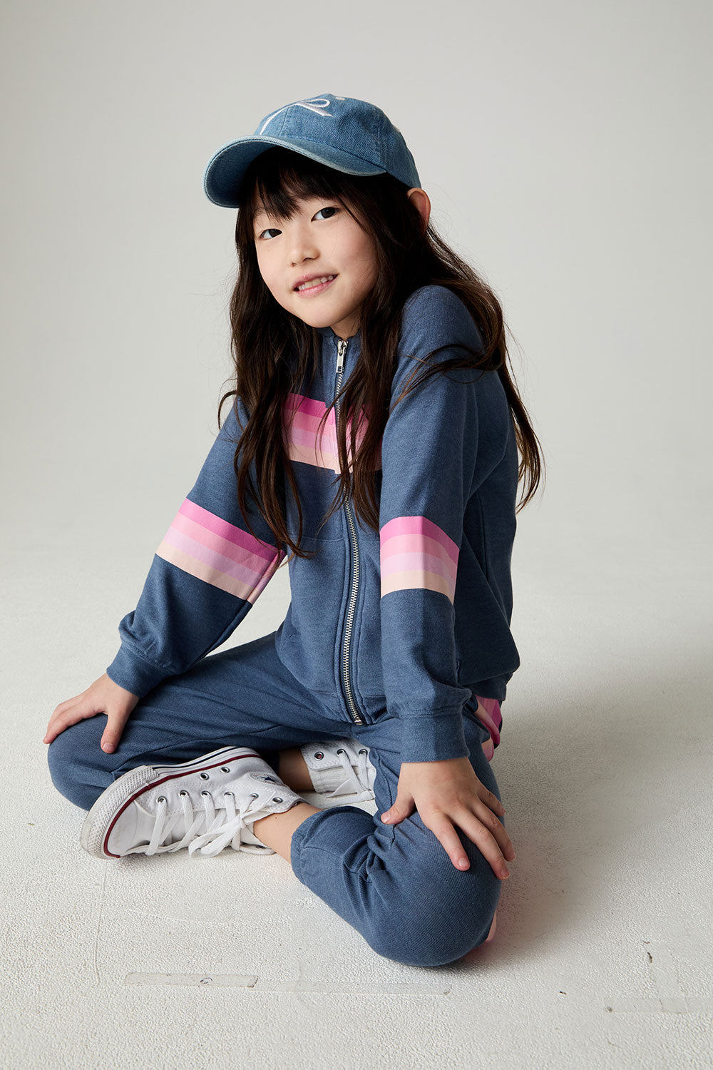 Front view of a seated girl wearing the Chaser Multi Stripes Girls Hoodie on a neutral background with hat