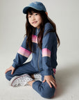 Front view of a seated girl wearing the Chaser Multi Stripes Girls Hoodie on a neutral background with hat