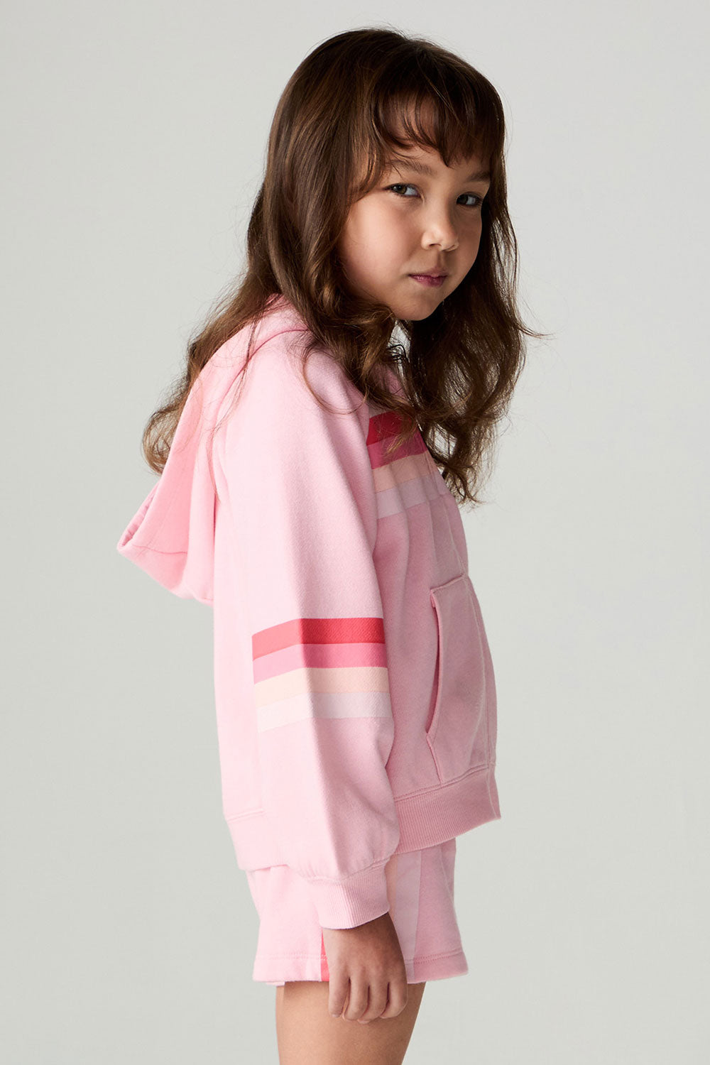 Side view of a girl wearing the Chaser Multi Stripes Girls Zip Up on a neutral background with shorts