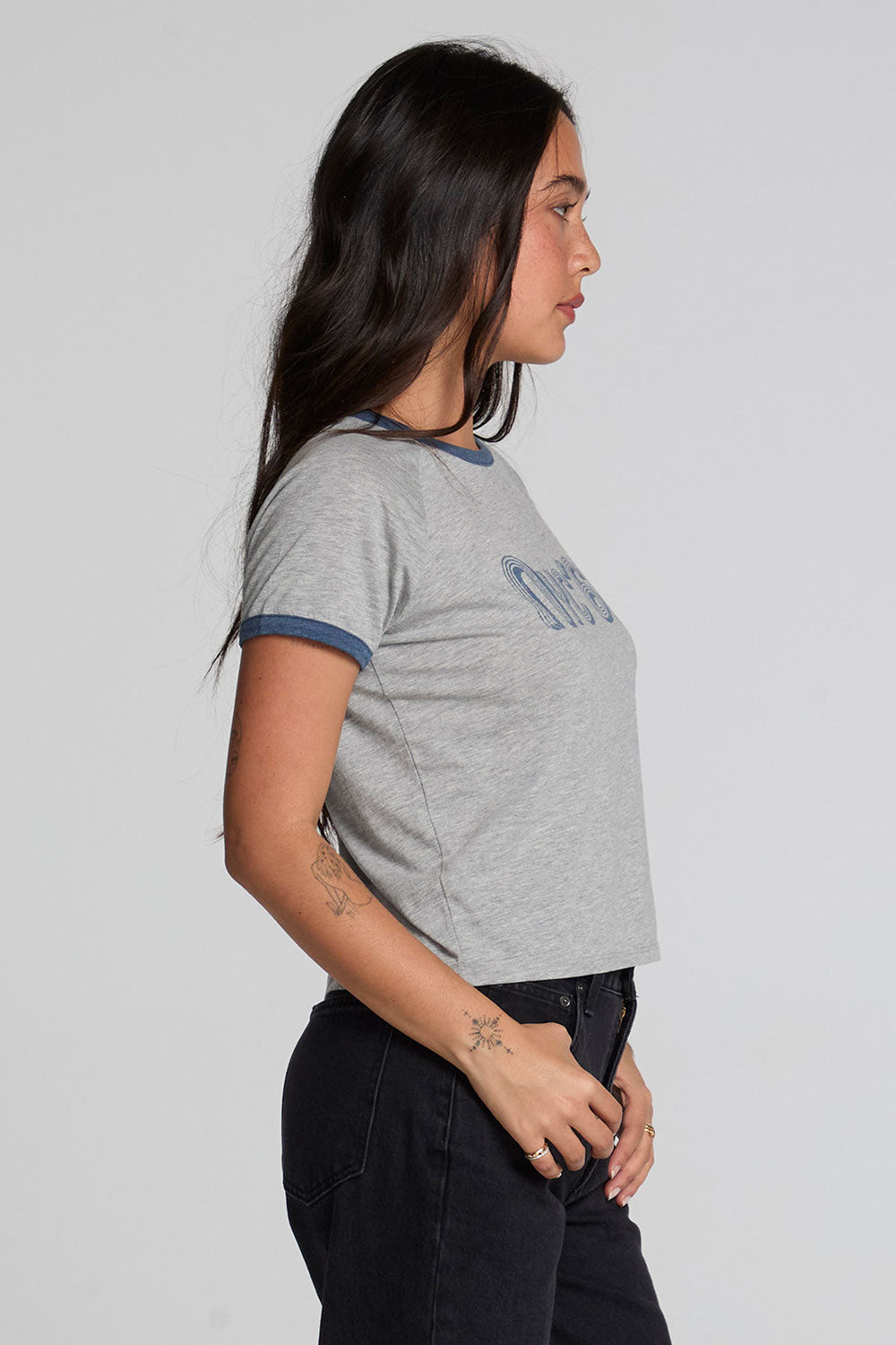 Side view of a woman wearing the Chaser NYC 68 Ringer Graphic Tee and black jeans on a neutral background 
