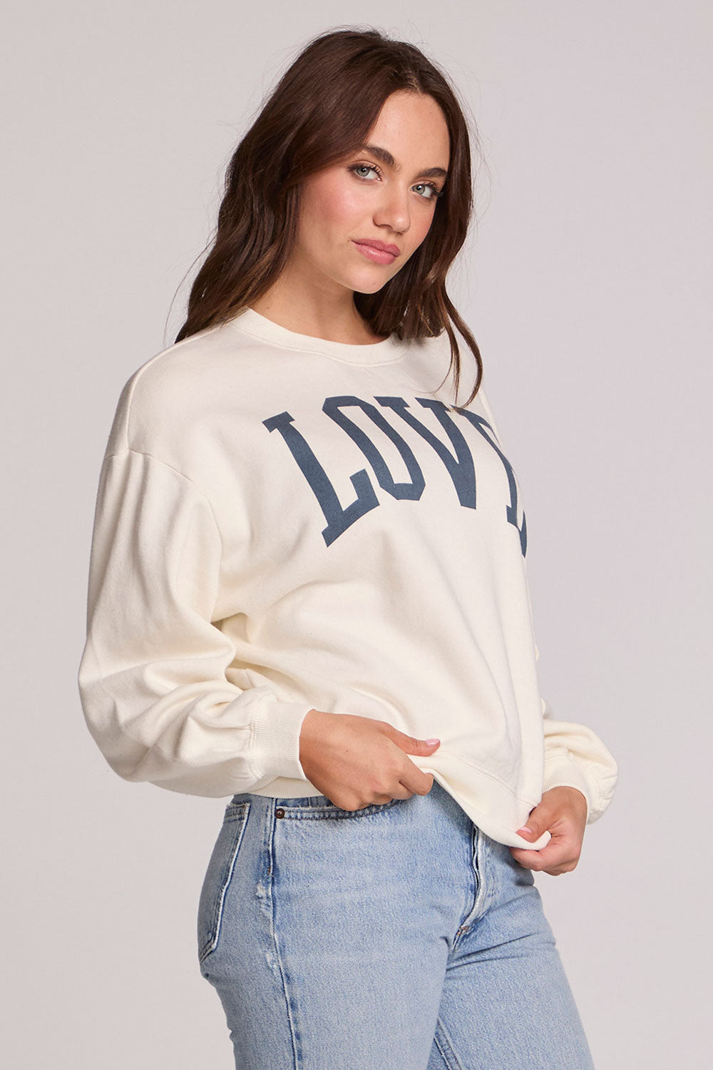 Side angle view of a woman wearing the Chaser Navy Love Pullover Sweater and jeans on a neutral background 