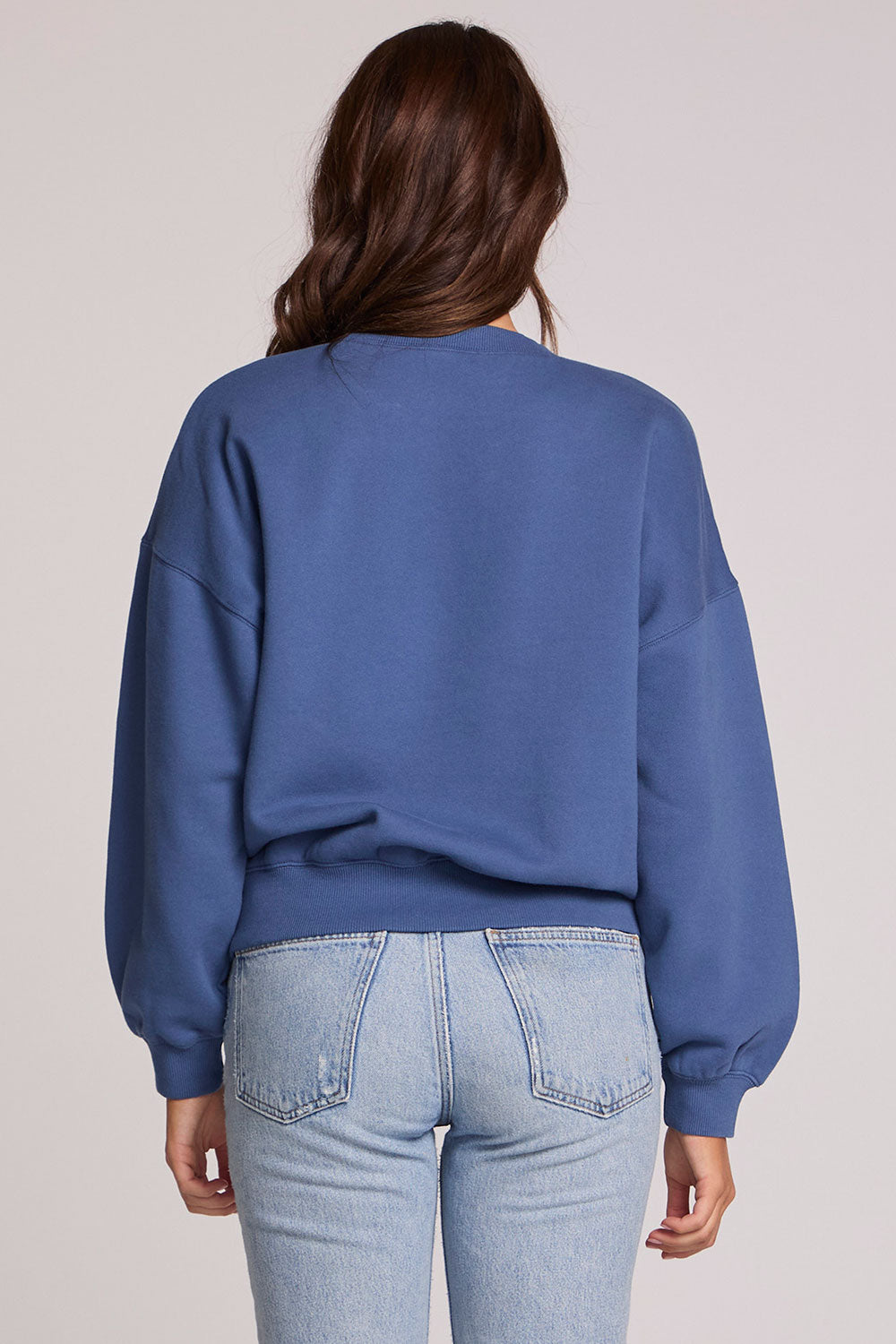 Back view of a woman wearing the Chaser New York Long Sleeve on a neutral background with arms lowered