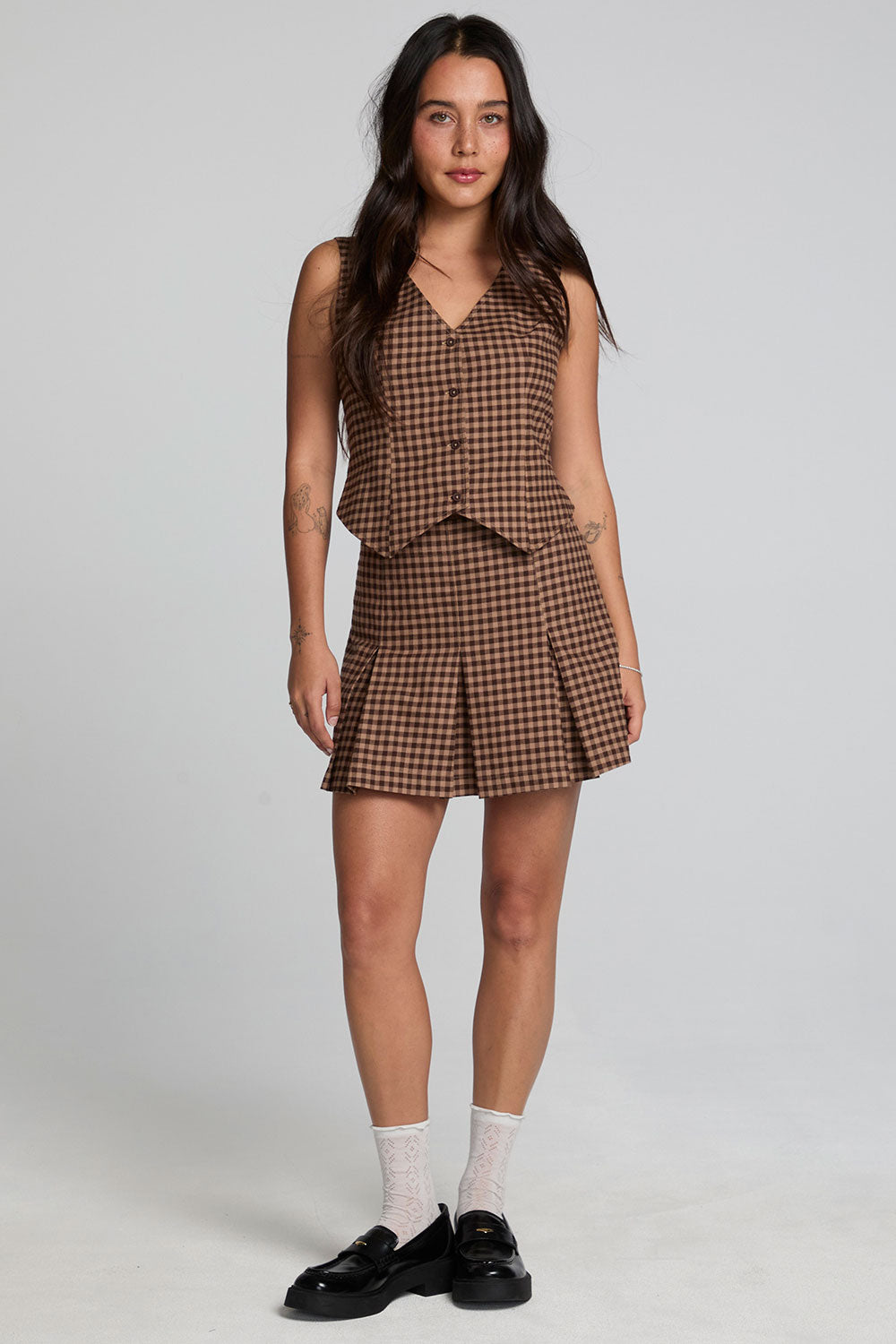 A full body front view of a woman wearing the Chaser Pea Choco Check Waistcoat and white socks on a neutral background