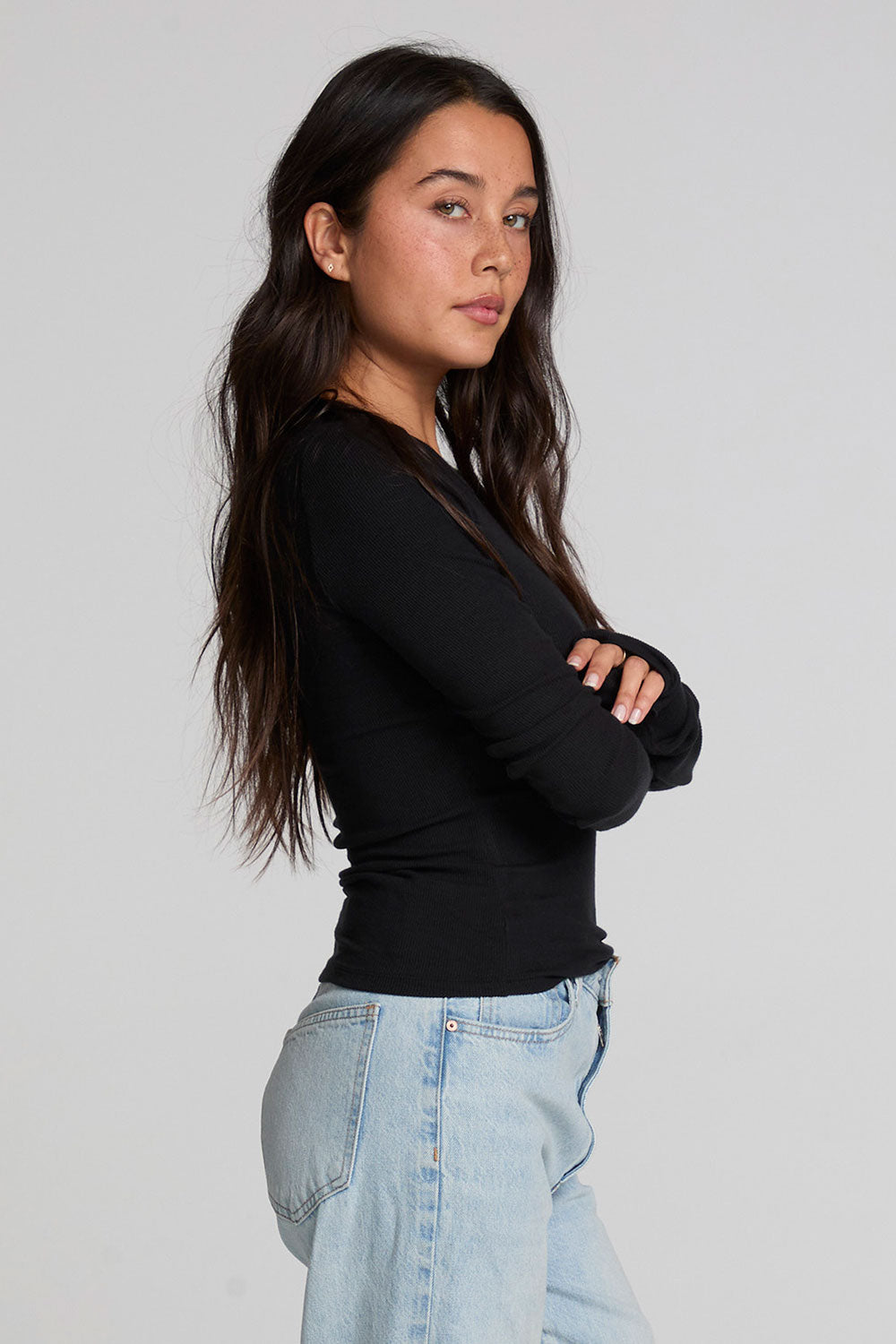 Side view of a woman wearing the Chaser Porta Black Long Sleeve on a neutral background with jeans