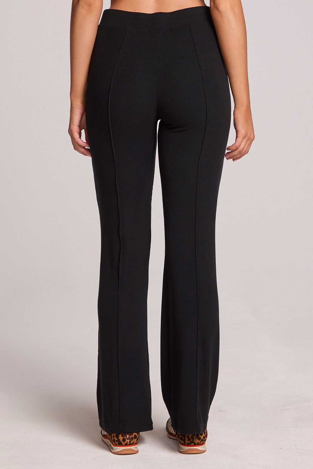 Back view of a woman wearing the Chaser Rhose Black Pants on a neutral background with arms lowered down sides