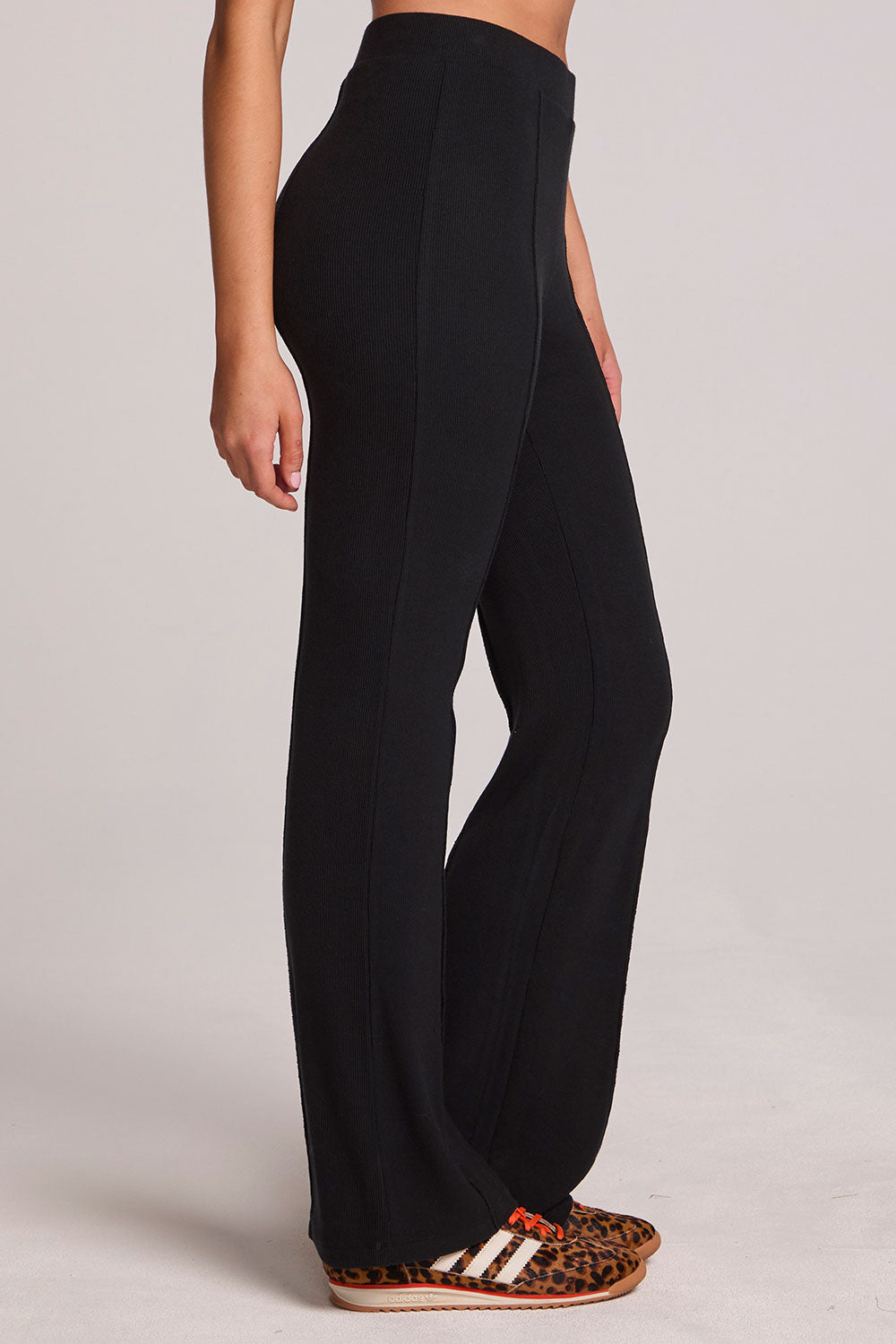 Side view of a woman wearing the Chaser Rhose Black Pants on a neutral background with arms lowered at sides