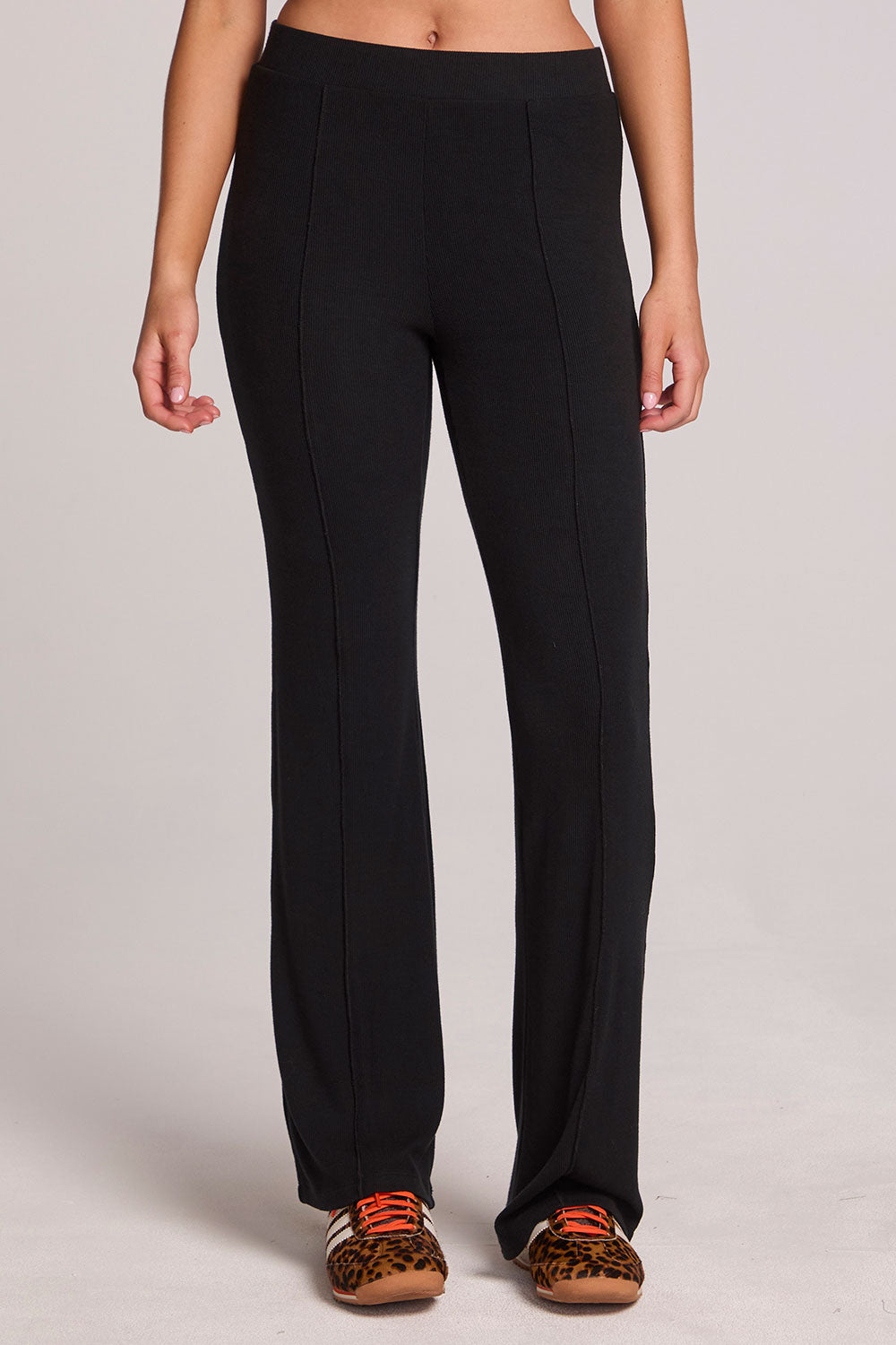 A full body front view of a woman wearing the Chaser Rhose Black Pants on a neutral background with arms at sides