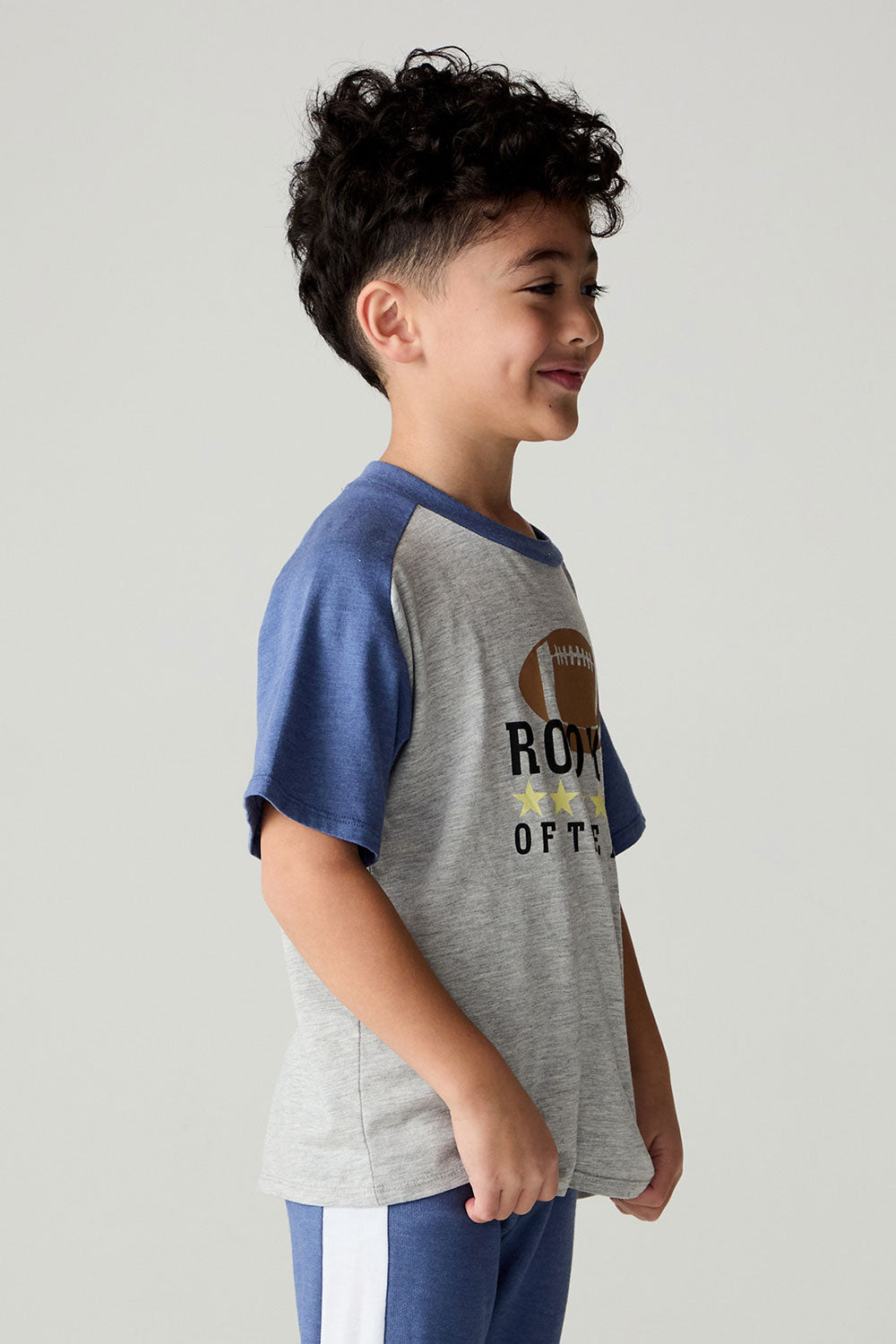 Side view of a boy wearing the Chaser Rookie Boys Tee on a neutral background with arms at sides and blue pants