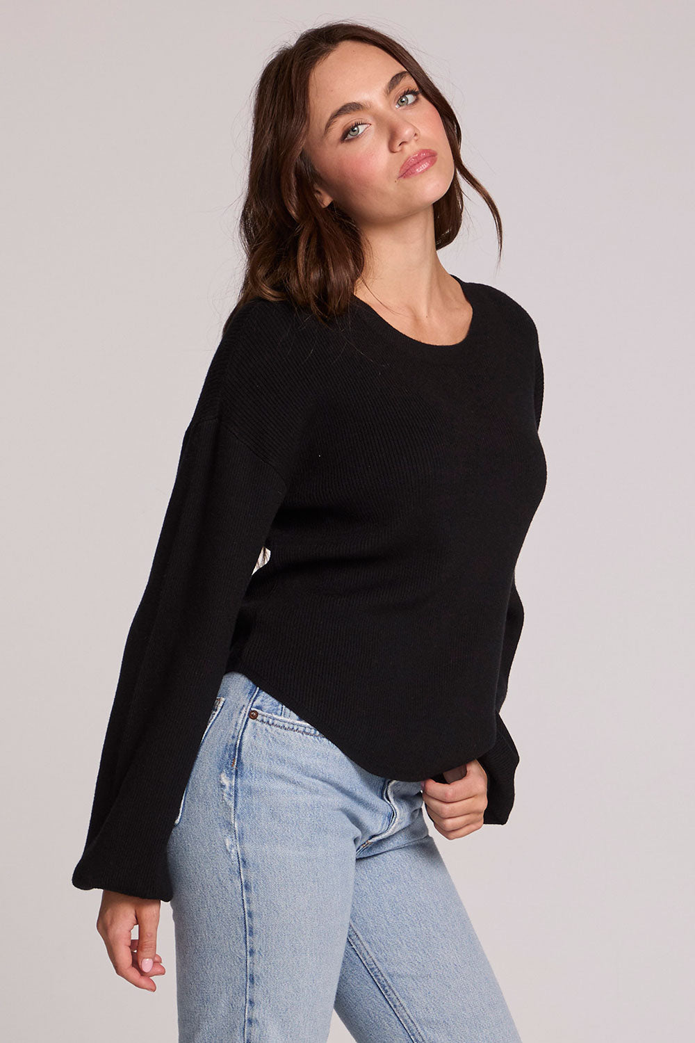 Side view of a woman wearing the Chaser Ruthy Black Fullsleeve Top on a neutral background with jeans and hand on hem