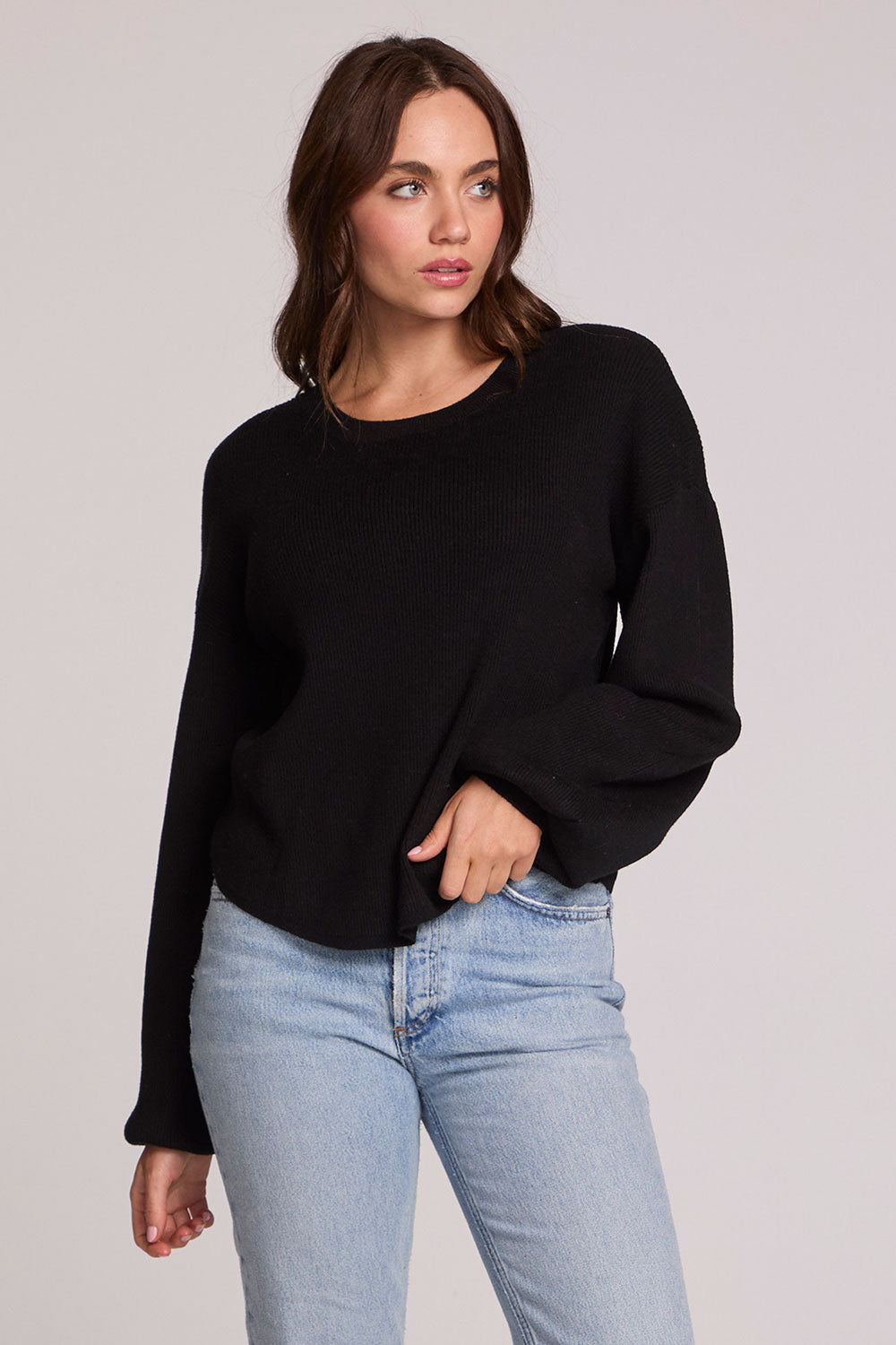 Front view of a woman wearing the Chaser Ruthy Black Fullsleeve Top on a neutral background with jeans, one hand on hem and another in pocket