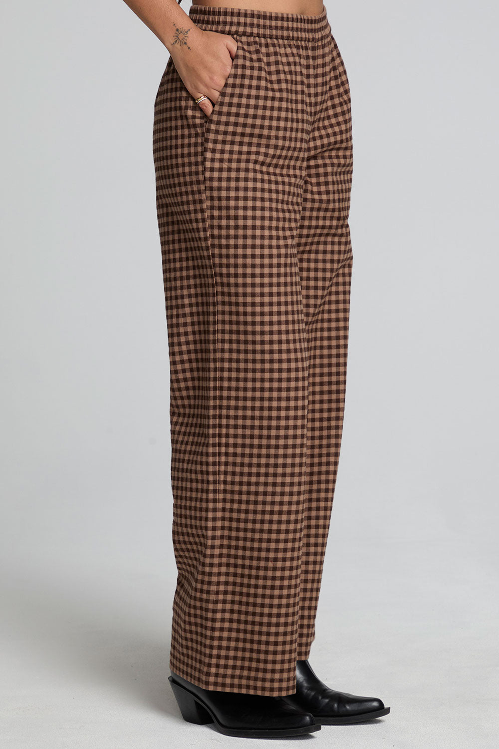 Side view of a woman wearing the Chaser Seren Choco Check Pants on a neutral background with hands in pockets