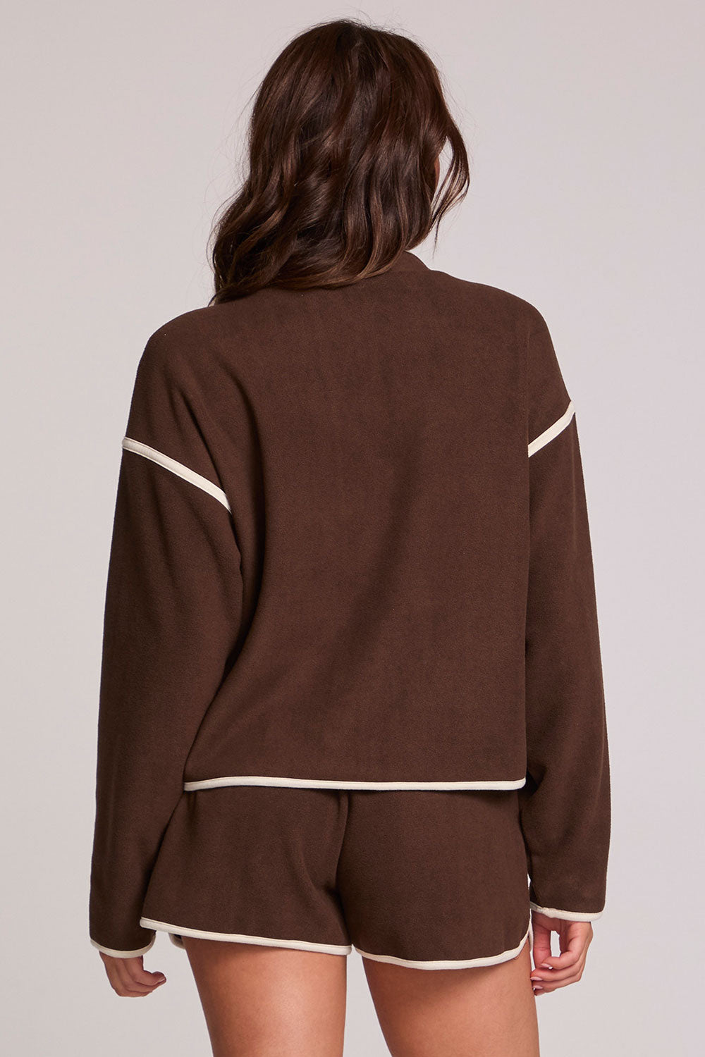 Back view of a woman wearing the Chaser Sharun Worn Brown Jacket on a neutral background with matching brown shorts