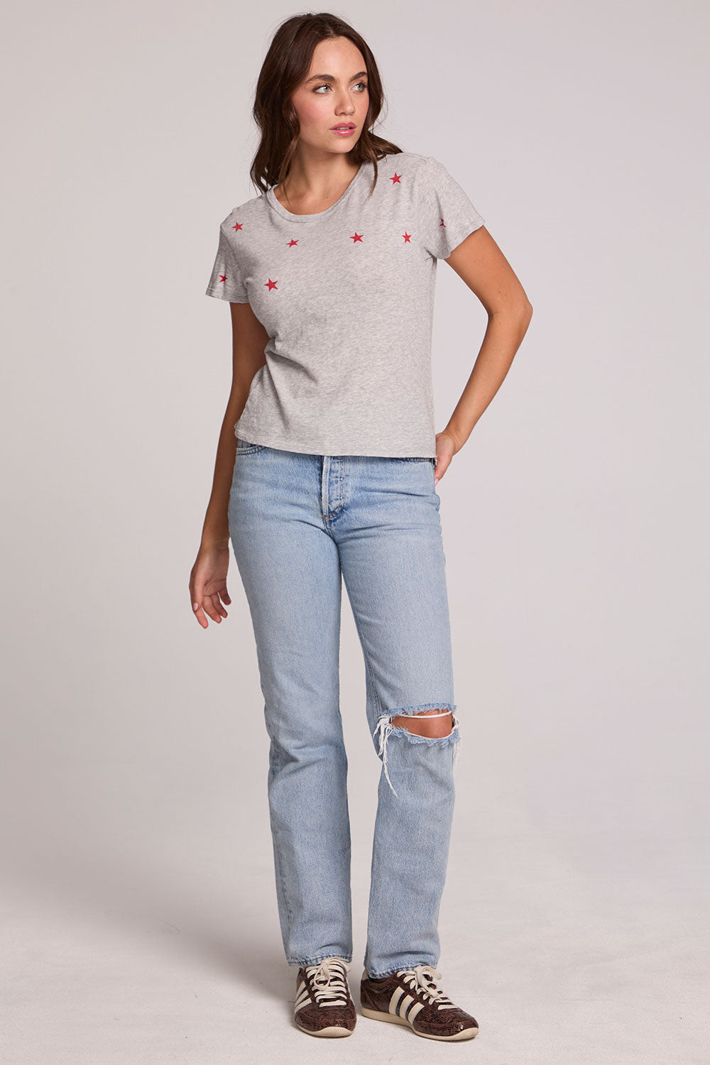 Full body view of a woman wearing the Chaser Star Setter Cropped Tee on a neutral background with ripped blue jeans 