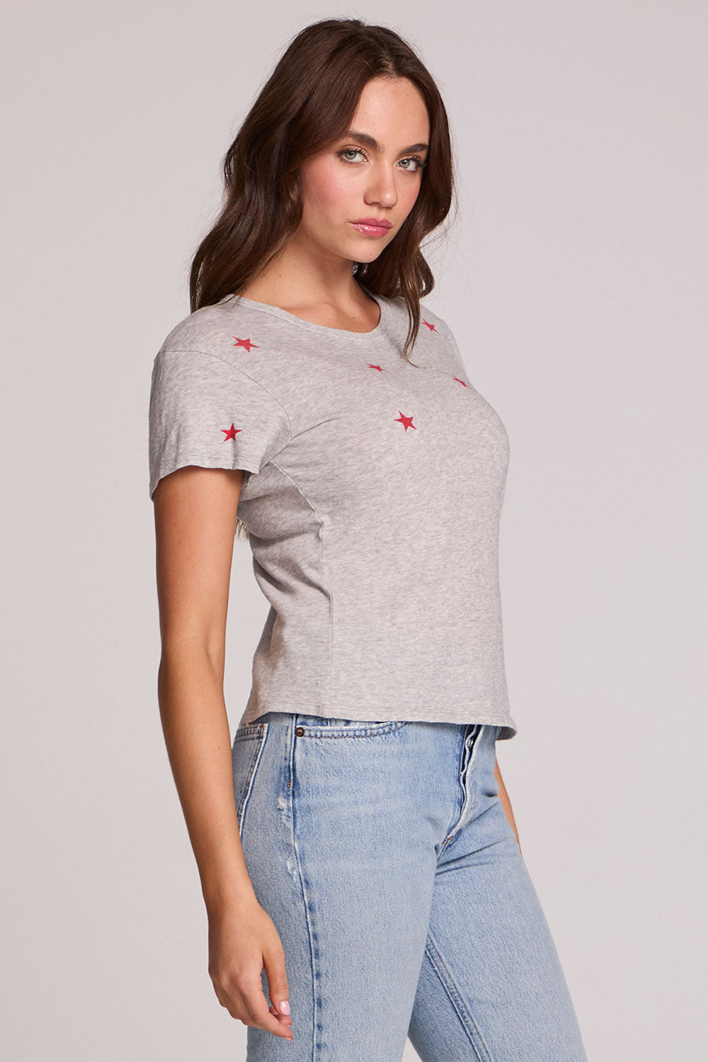 Side angle view of a woman wearing the Chaser Star Setter Cropped Tee on a neutral background with jeans 