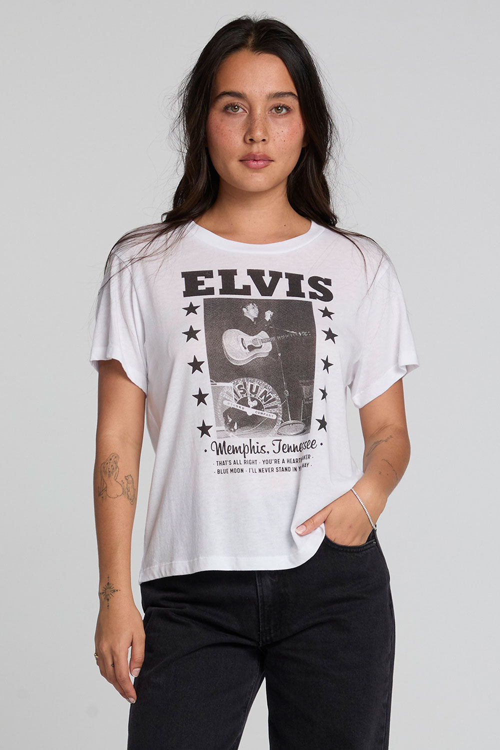 Front view of a woman wearing the Chaser Sun Records Elvis 1972 Tee on a neutral background with arms at sides and black pants