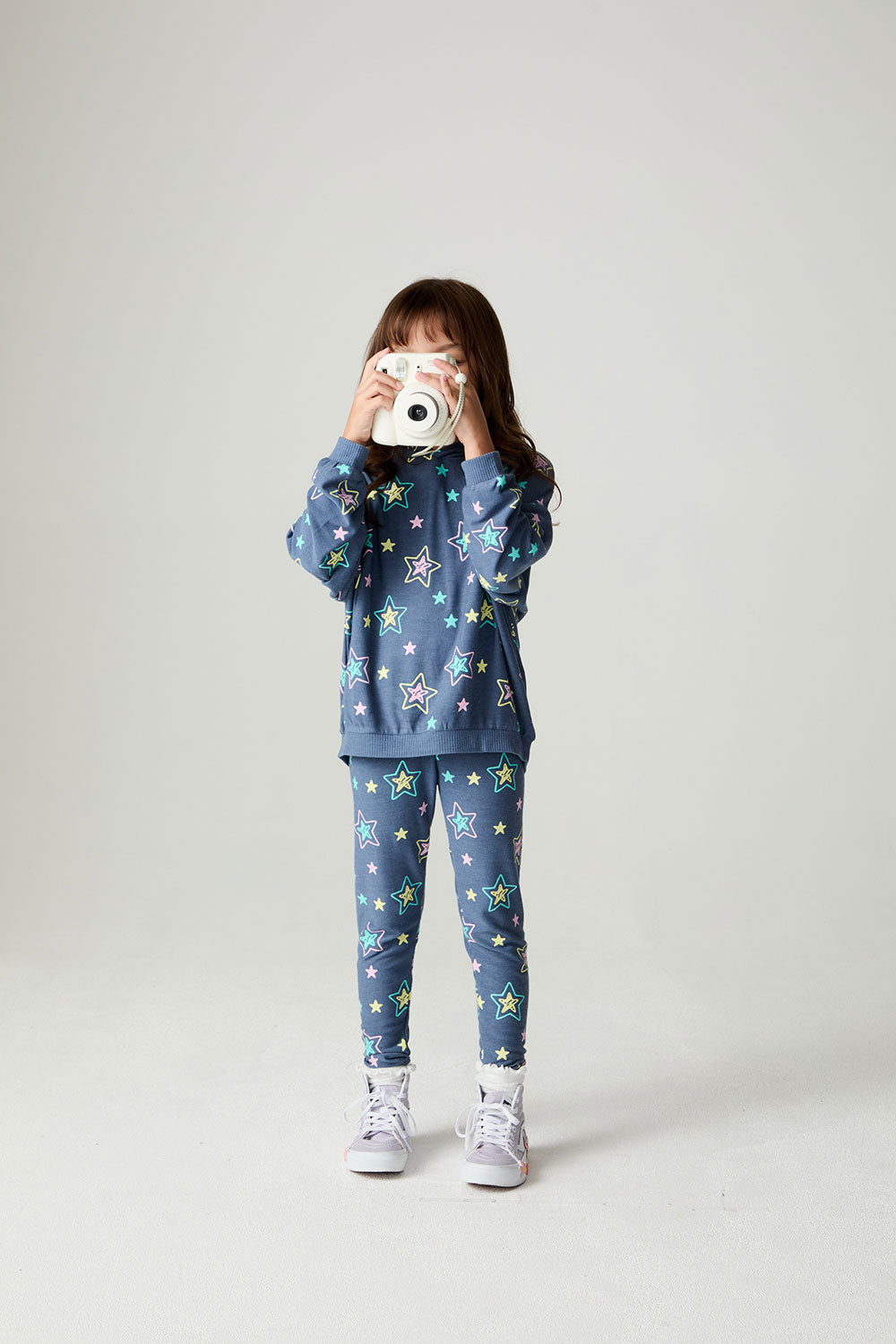 Front view of a girl wearing the Chaser Super Star Girls Zip Up on a neutral background holding a camera
