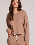 Front view of a woman wearing the Chaser Suzzans Camel Cropped Sweatshirt and matching pants on a neutral background with one hand on waistband