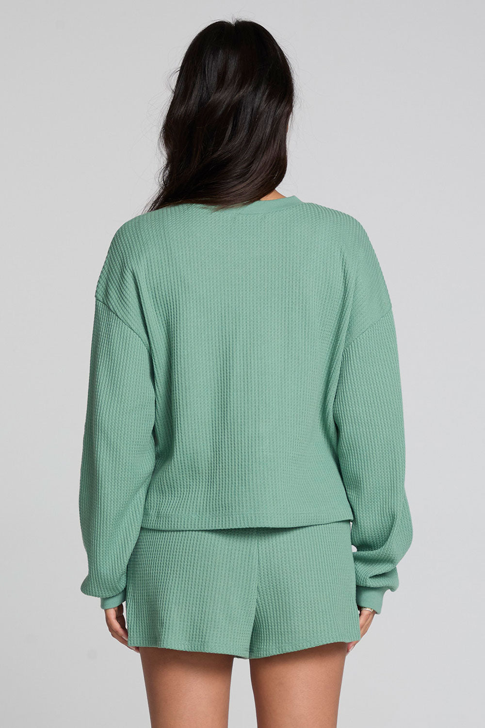 Back view of a woman wearing the Chaser  Suzzans Verdelle Sweatshirt on a neutral background with shorts