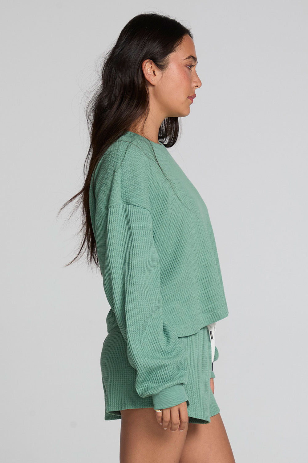 Side view of a woman wearing the Chaser  Suzzans Verdelle Sweatshirt on a neutral background with matching shorts