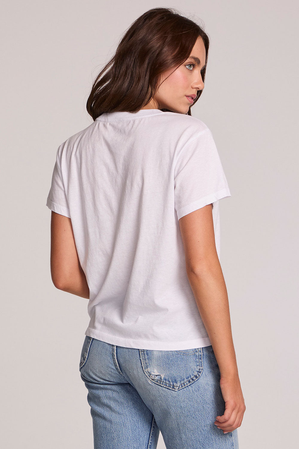 Back view of a woman wearing the Chaser  The Best Cropped Graphic Tee and blue jeans on a neutral background