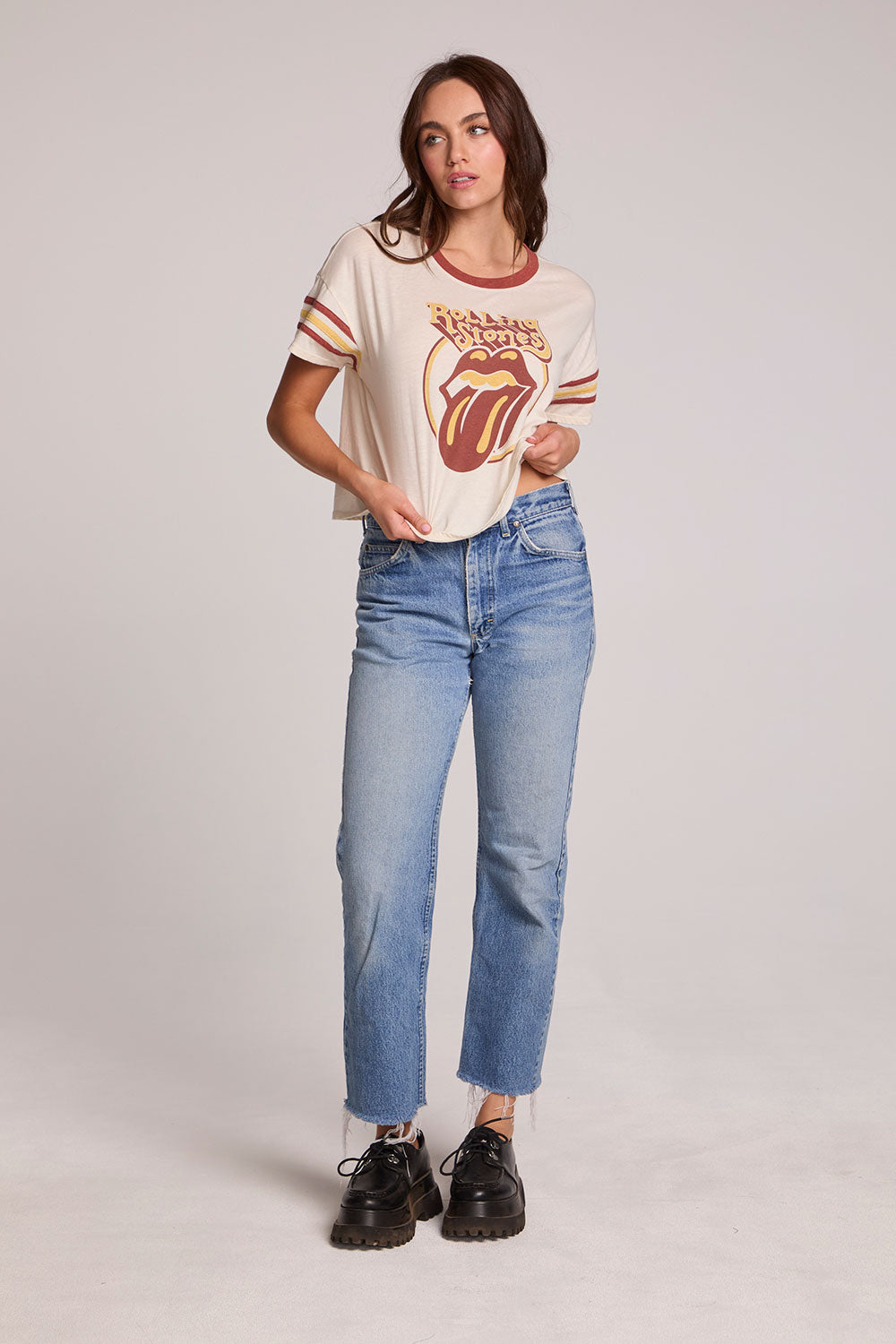 Full body front view of a woman wearing the Chaser  The Rolling Stones Retro Tongue Tee on a neutral background with jeans and hands on hips