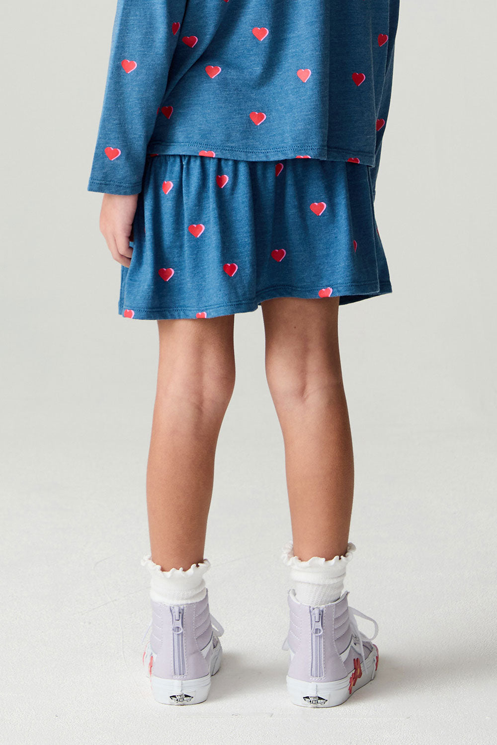 Back view of a girl wearing the Chaser Tiny Hearts Girls Skirt on a neutral background