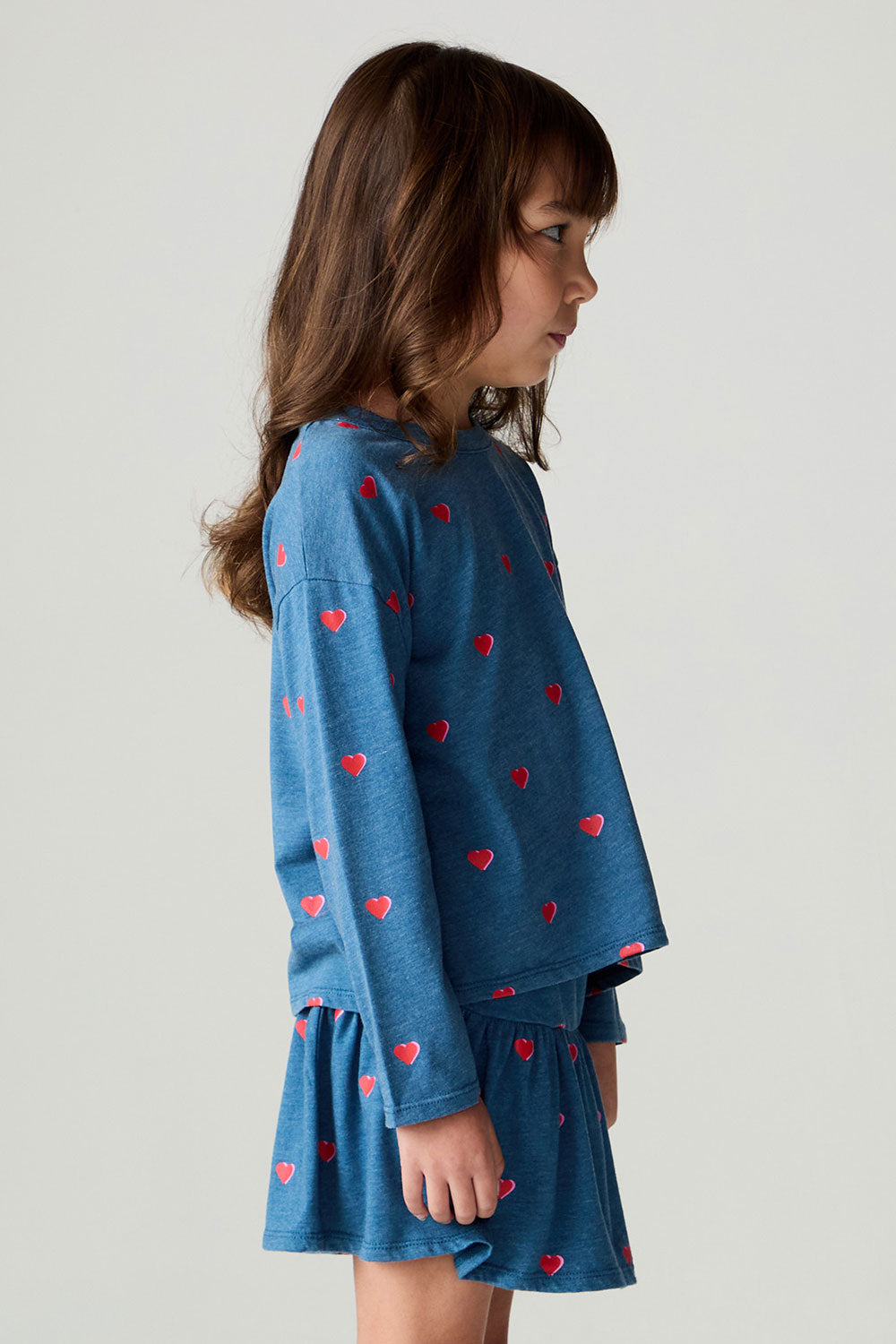 Side view of a girl wearing the Chaser Tiny Hearts Girls Tee on a neutral background with arms at sides